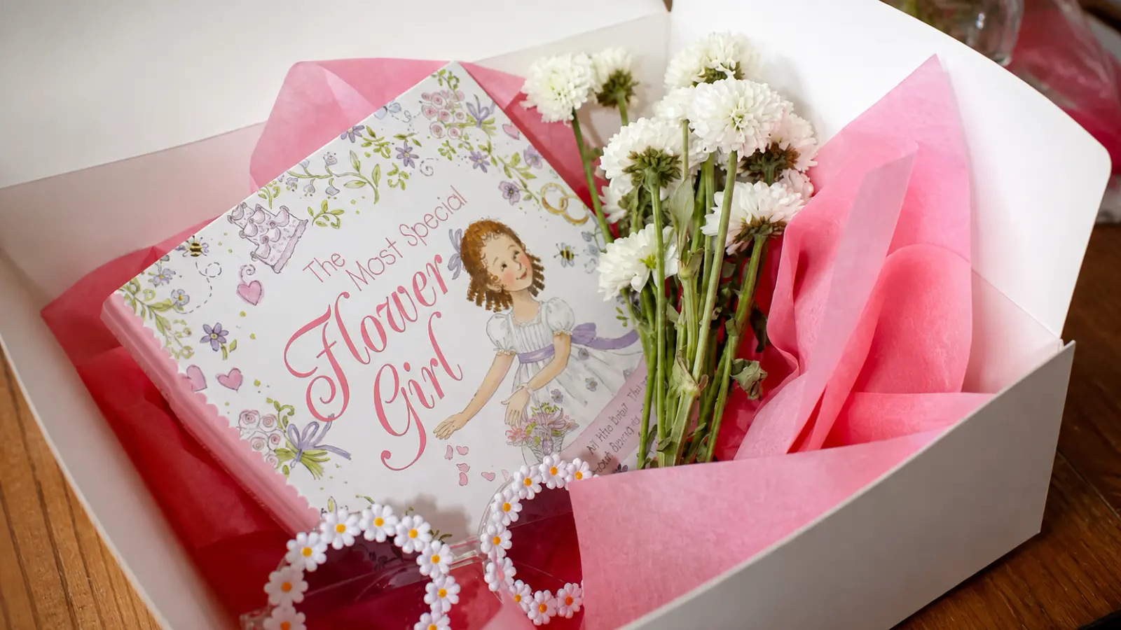 Flower girl proposal gift arranged in a white box with a flower girl book, fresh white flowers, pink tissue paper, and accessories