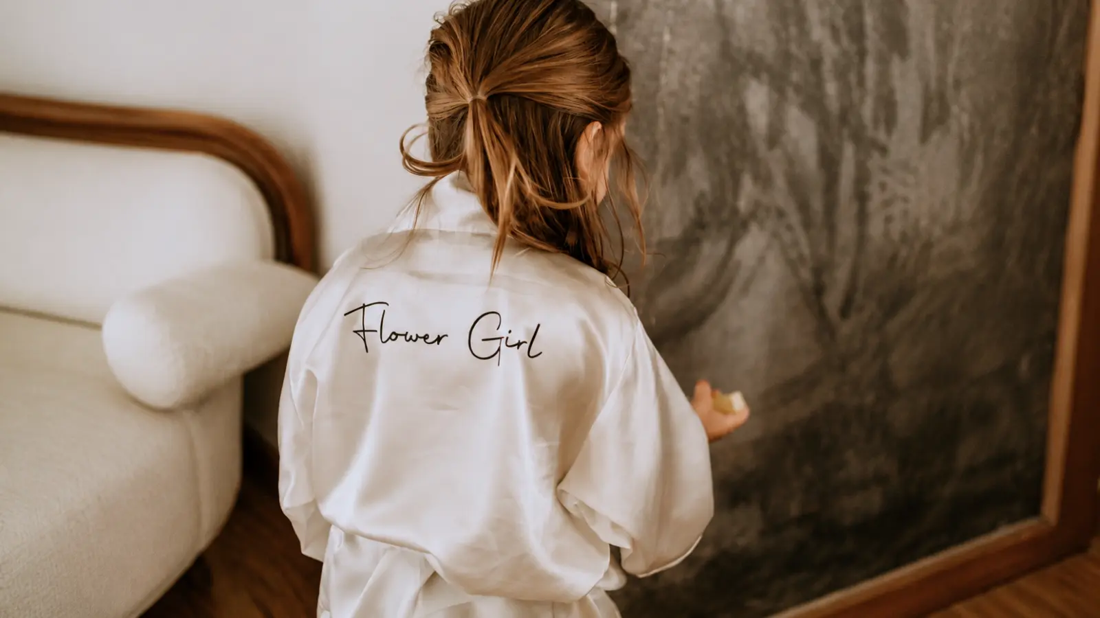Flower girl wearing a personalized white satin robe with Flower Girl lettering across the back while getting ready for the wedding Flower Girl Gifts and Proposal Ideas