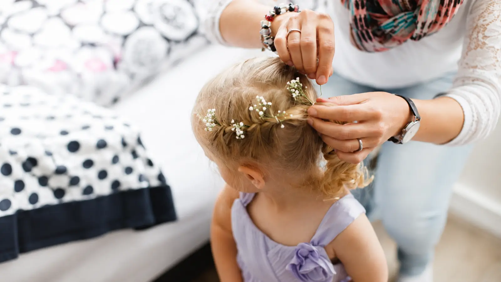 Flower girl hairstyle with blonde hair arranged in a braided updo as small white flowers are carefully added throughout the braids