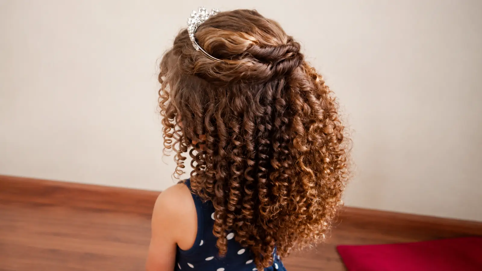 Flower girl hairstyle with defined brown ringlets, twisted sections across the crown, and a delicate silver tiara worn as a wedding hair accessory