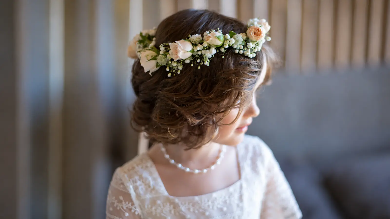Flower girl hairstyle with a soft brown updo and fresh flower crown featuring blush roses, greenery, and small white flowers for a wedding