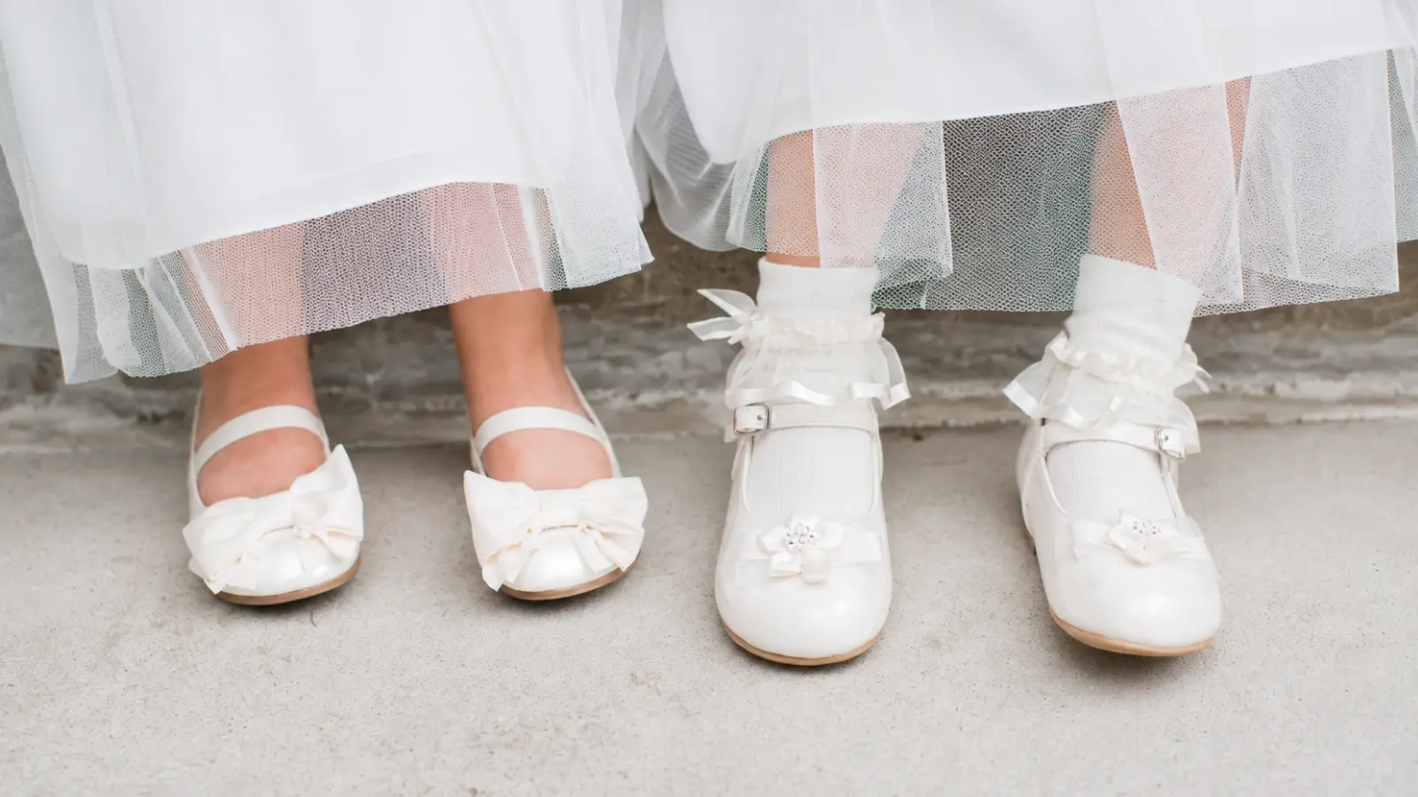 Flower girl shoes in white with bow and floral details paired with tulle dresses and decorative socks for a classic wedding look