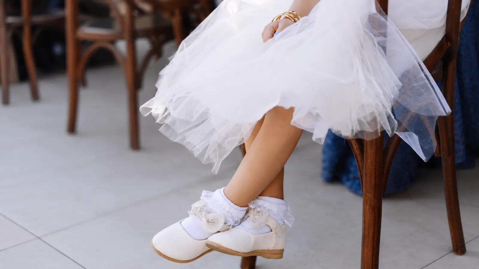 lower girl shoes in white flats worn with decorative ruffled socks and a layered tulle dress while seated at a wedding