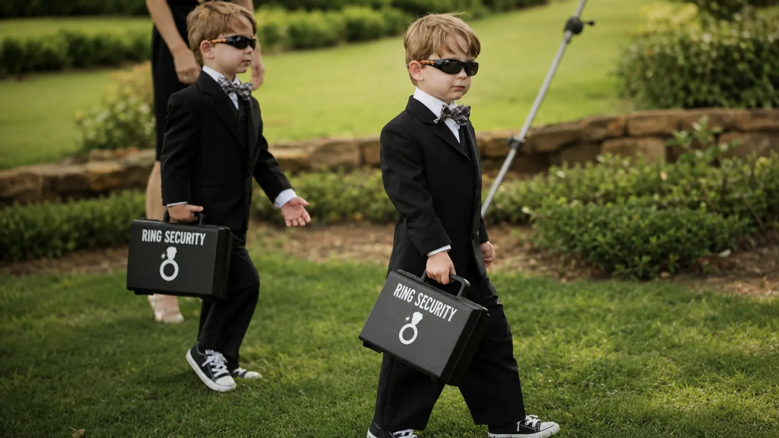 Two ring bearers in black suits and sunglasses carrying Ring Security cases for a funny and memorable wedding ceremony entrance