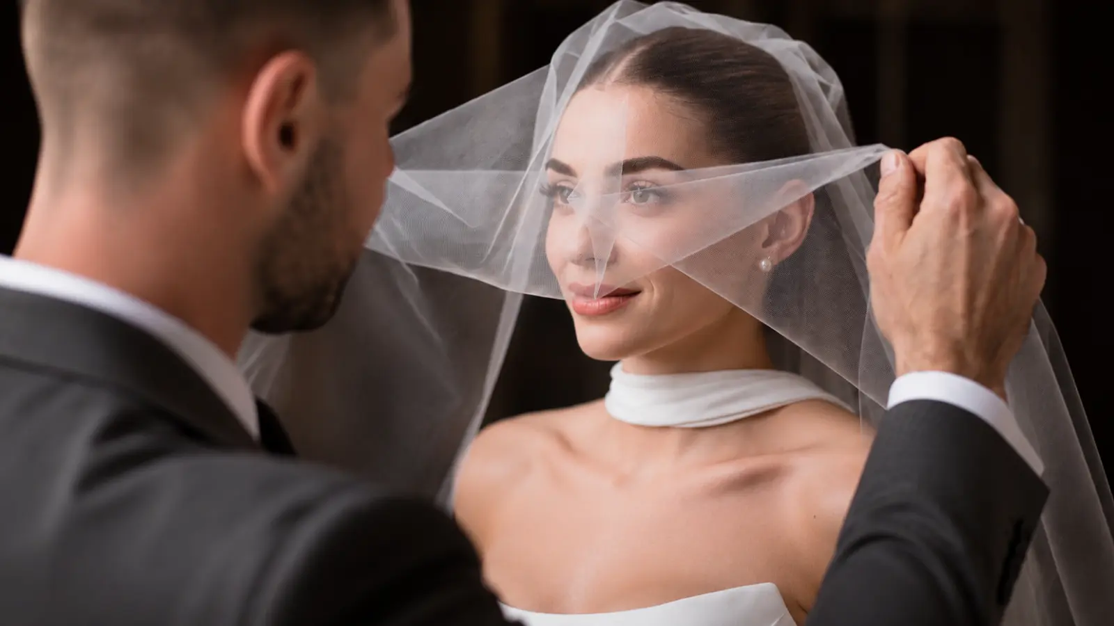 Groom lifting a sheer blusher wedding veil from the bride’s face during a traditional ceremony moment before the couple stands together