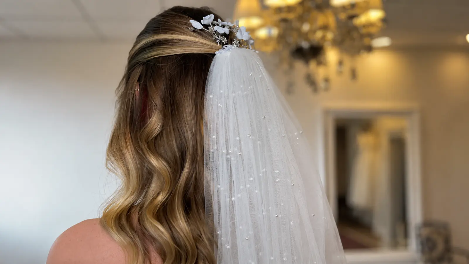 Highlighted half up half down wedding hair with a pearl-detailed veil secured beneath a delicate white floral bridal hair accessory Half Up Half Down Wedding Hair With Veil