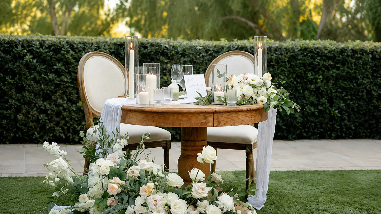 Head Table vs Sweetheart Table comparison represented by an intimate sweetheart table for two decorated with candles, greenery and white wedding flowers Head Table vs Sweetheart Table: Which Setup Is Right for Your Reception?