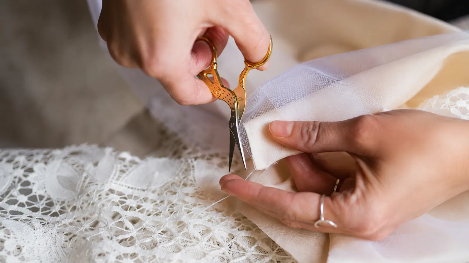 Hands carefully cutting white bridal tulle with small scissors while preparing and shaping the fabric for a handmade wedding veil