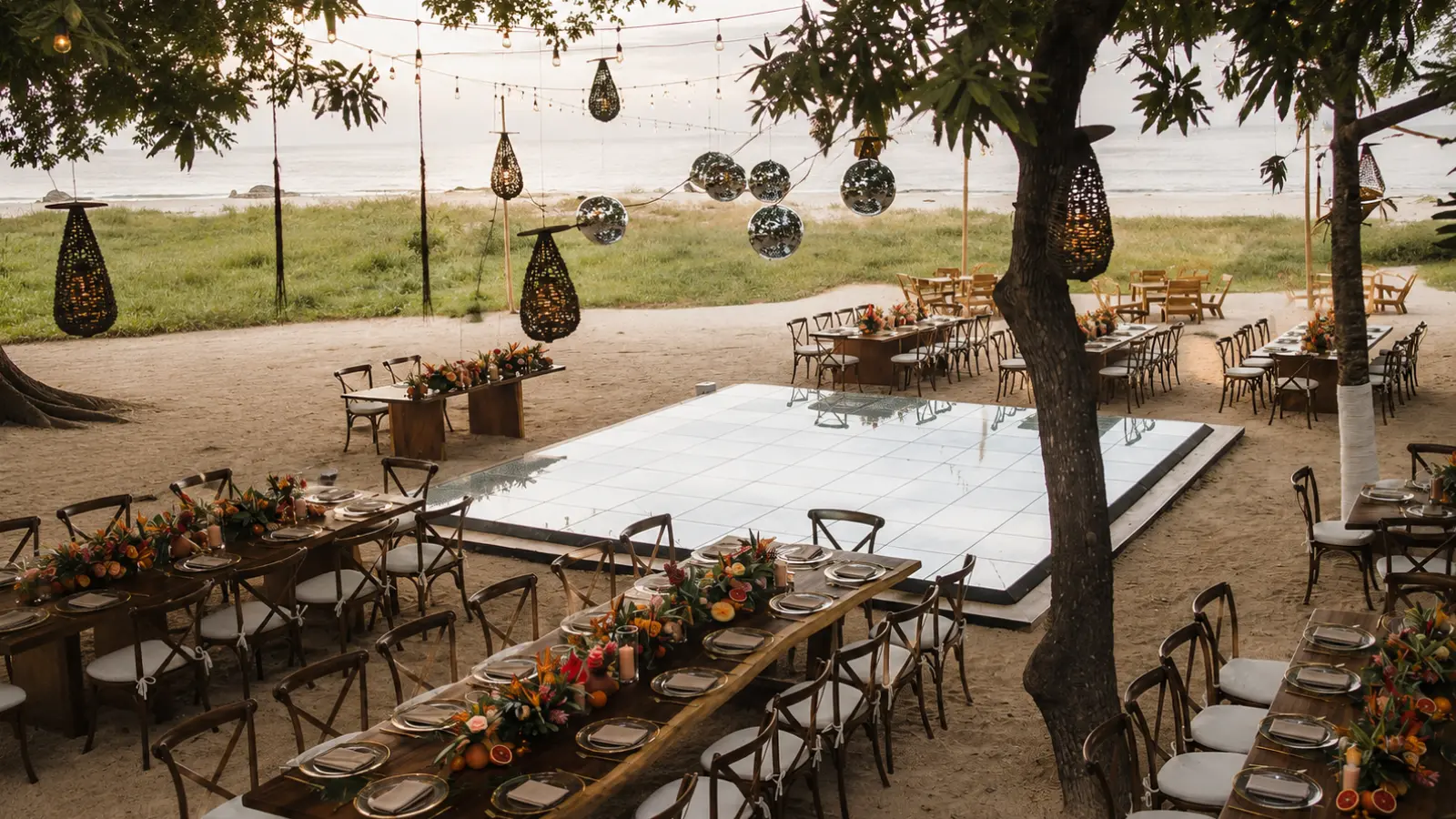 Beach wedding reception with decorated dining tables, floral centerpieces, hanging lights and a central dance floor overlooking the ocean
