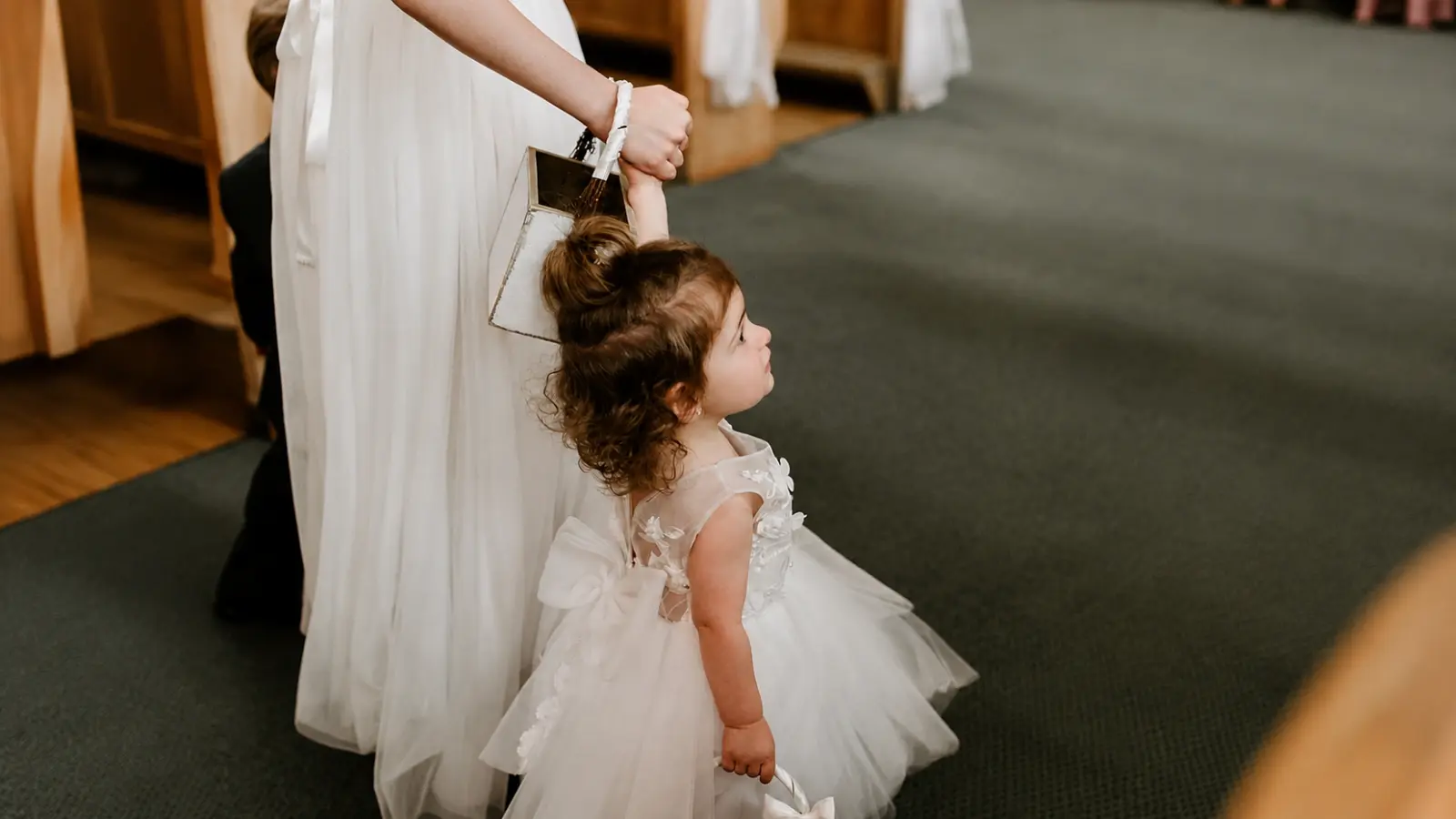 Young girl dressed for the wedding holds an adult’s hand during the ceremony, illustrating a meaningful way to include children in your wedding