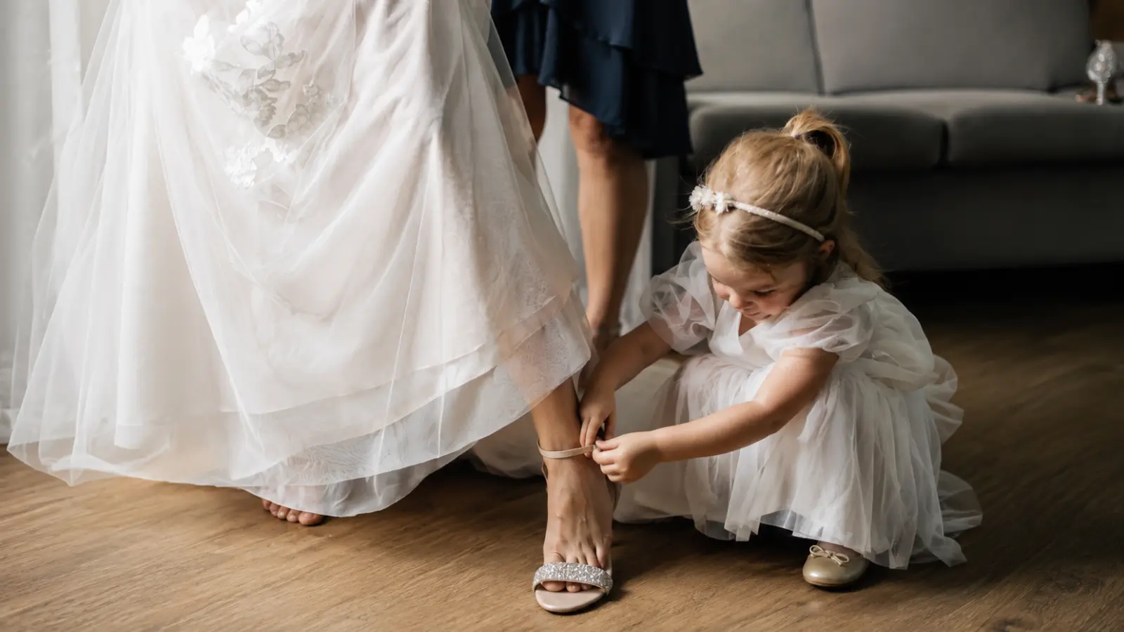 Young girl in a white dress helps the bride with her shoe, creating a meaningful getting-ready moment for children at the wedding