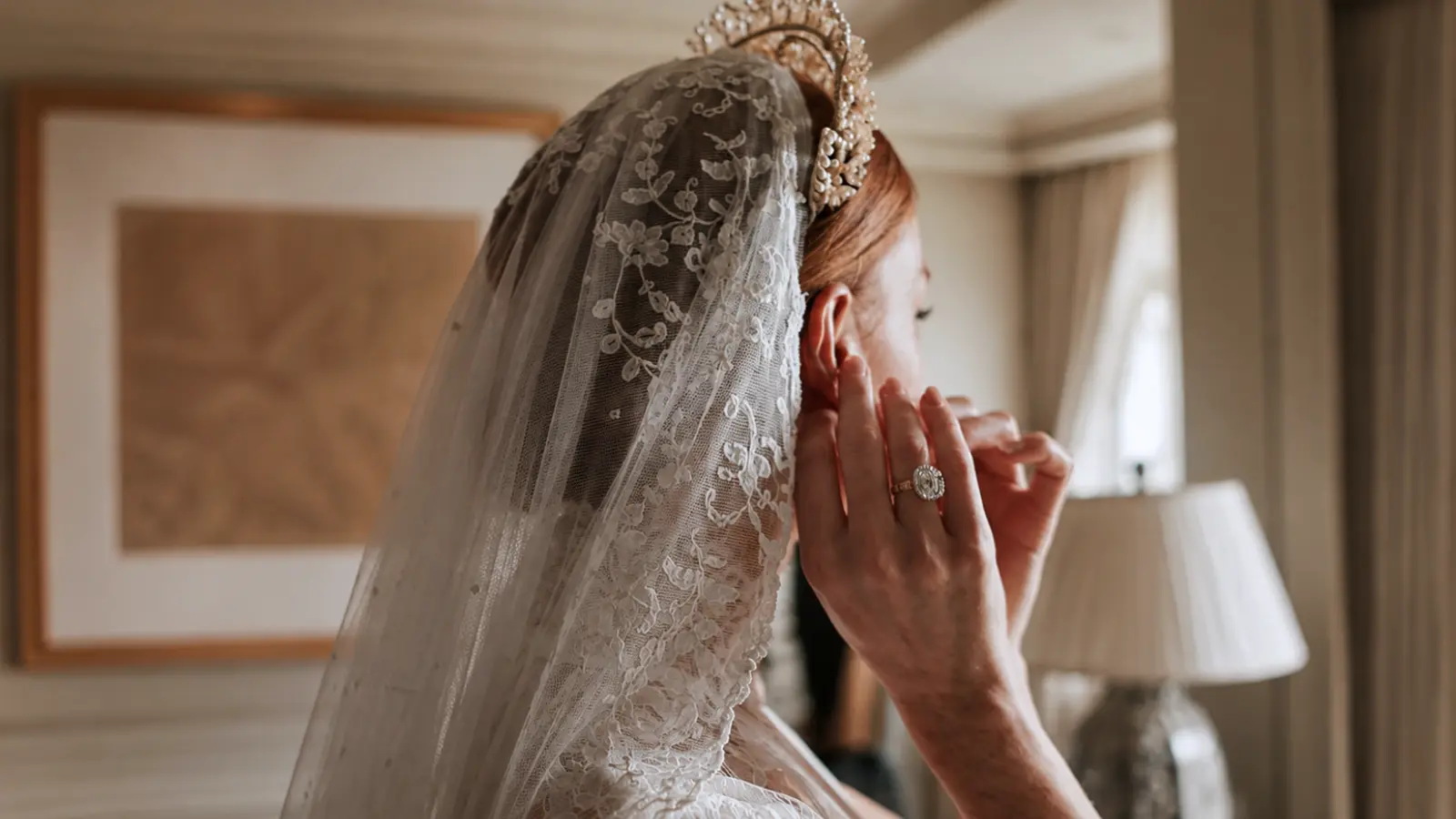 Bride wearing an embroidered lace wedding veil with an ornate crystal tiara positioned around a polished bridal updo