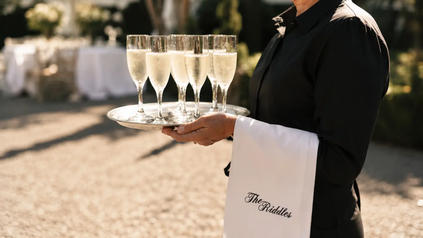 Wedding service professional carrying a tray of champagne glasses during an elegant outdoor luxury wedding reception