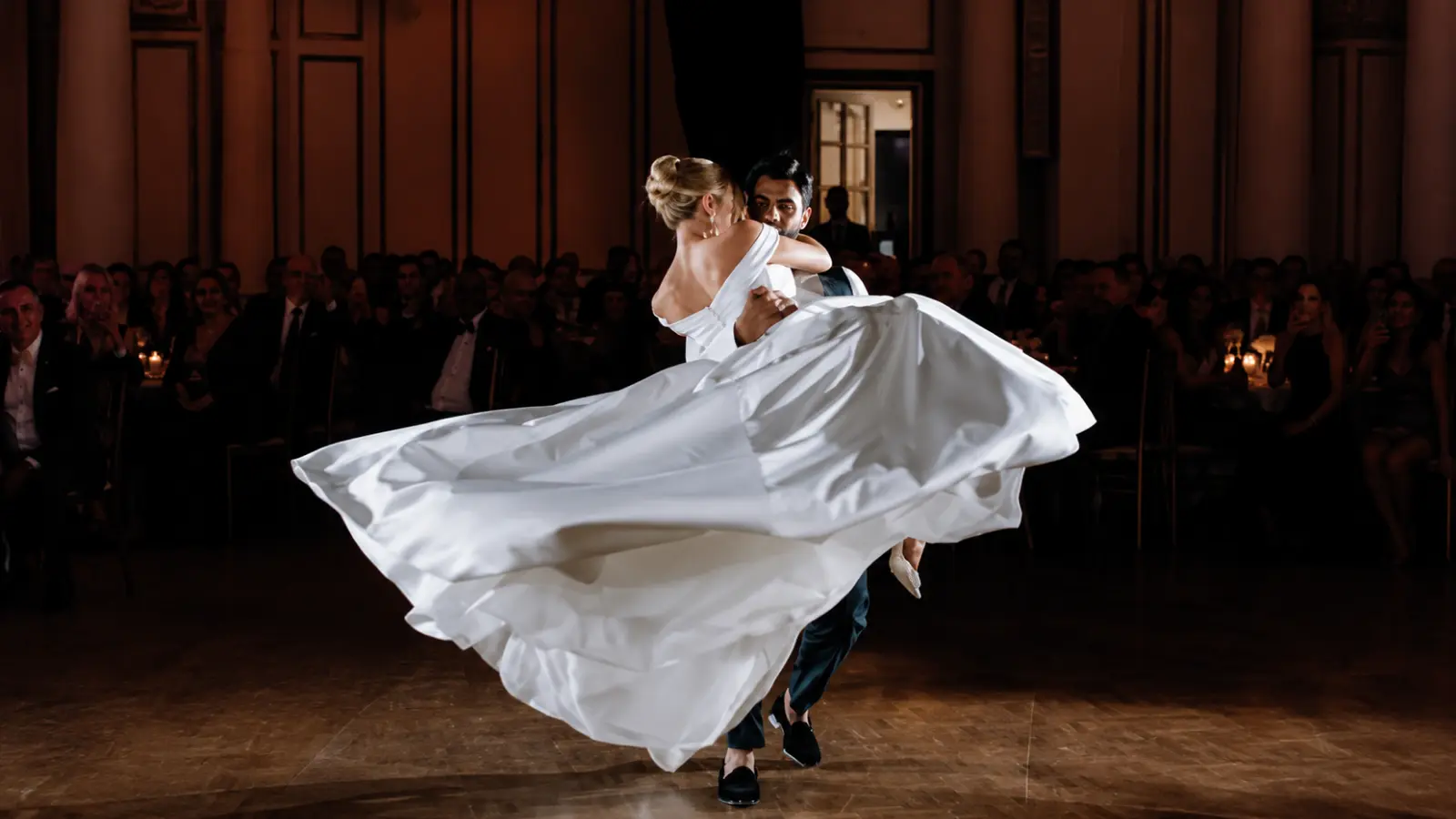 Multicultural newlywed couple performing their first dance at an elegant wedding reception while guests watch from surrounding tables