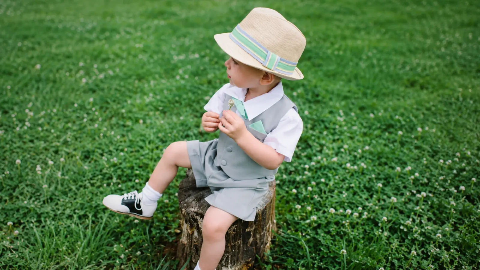 Little page boy wearing a gray vest, matching shorts, straw hat and two-tone shoes for a relaxed summer wedding outfit