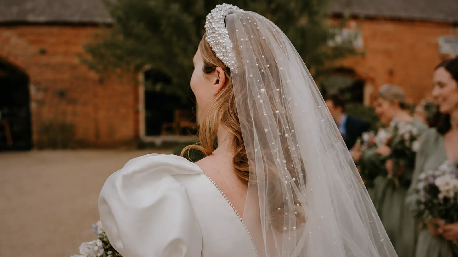 Bride shown from behind wearing a pearl wedding veil with a beaded bridal tiara and white wedding dress at an outdoor ceremony