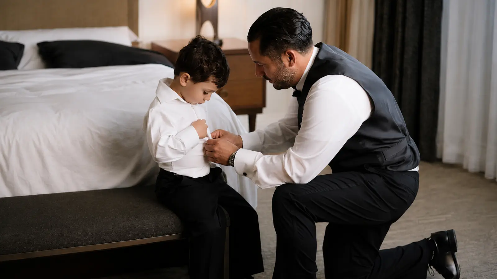 Older ring bearer getting ready in a tailored black suit, white dress shirt and black bow tie for a formal wedding ceremony