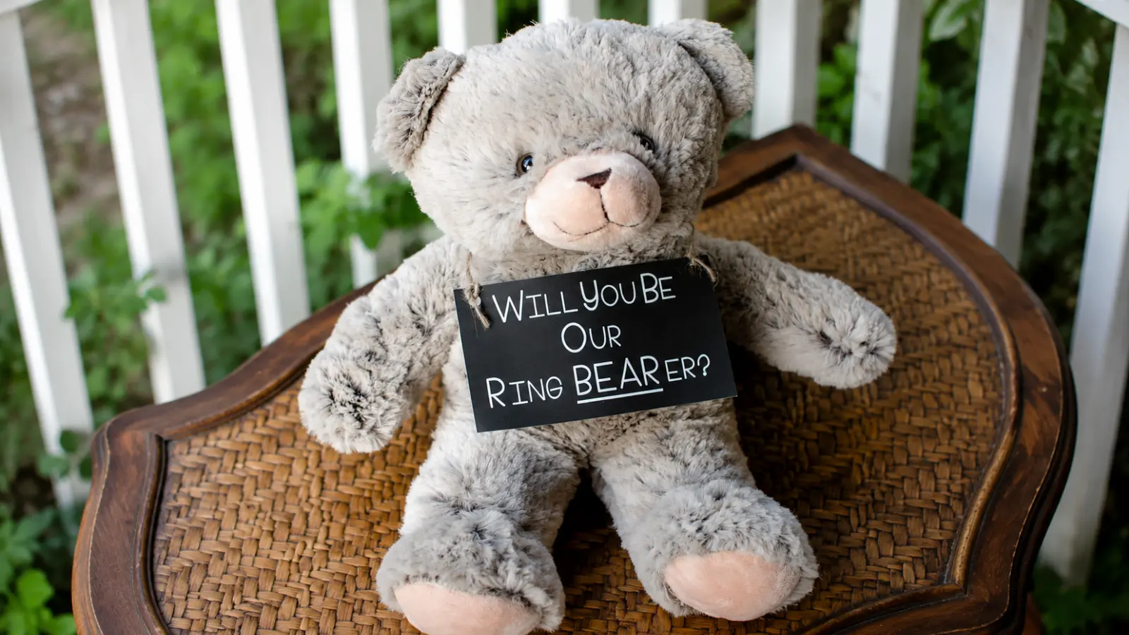 Teddy bear holding a Will You Be Our Ring Bearer sign as a cute proposal gift for asking a child to join the wedding