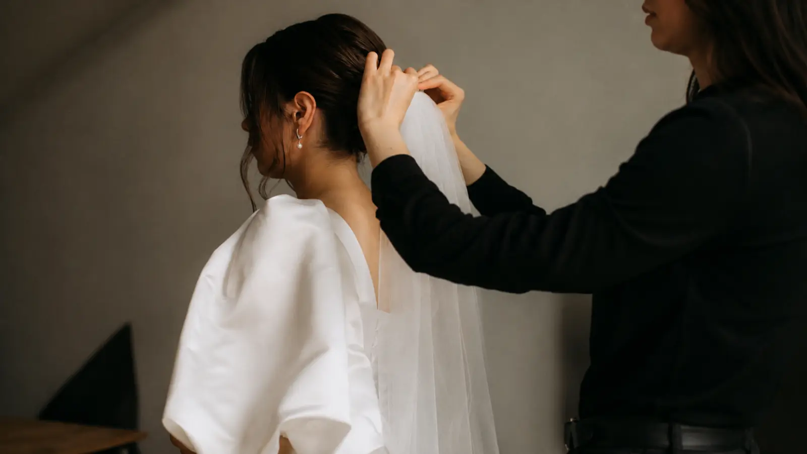 Bridal stylist attaching a simple wedding veil beneath a low updo while the bride prepares for her wedding ceremony