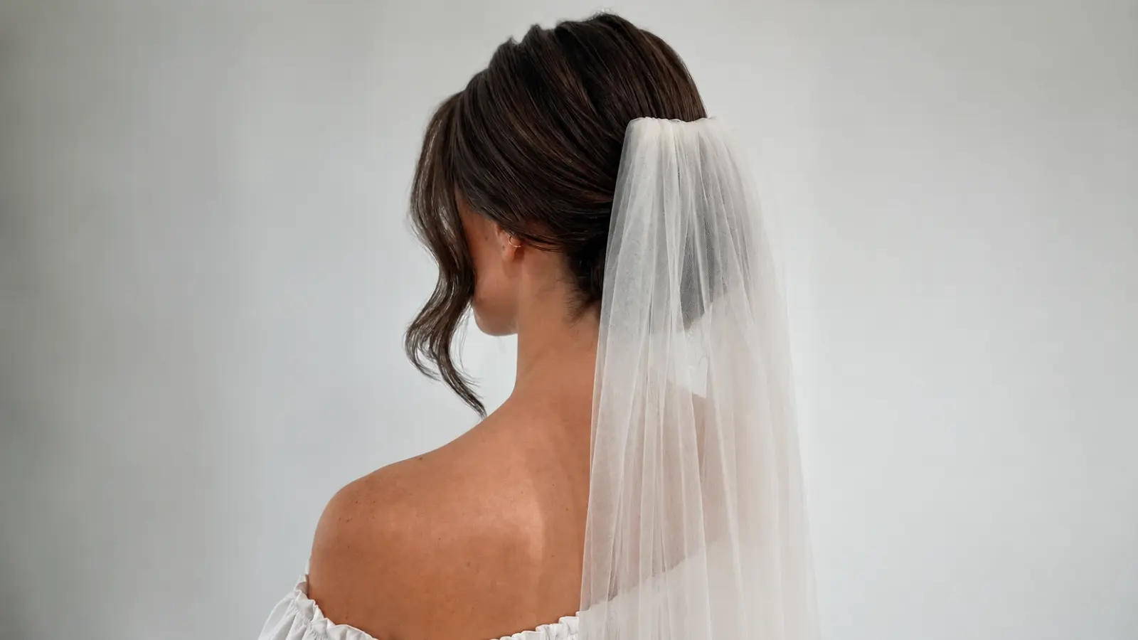 Bride wearing a simple wedding veil attached beneath a polished low updo with lightweight tulle falling smoothly down her back Simple Wedding Veils
