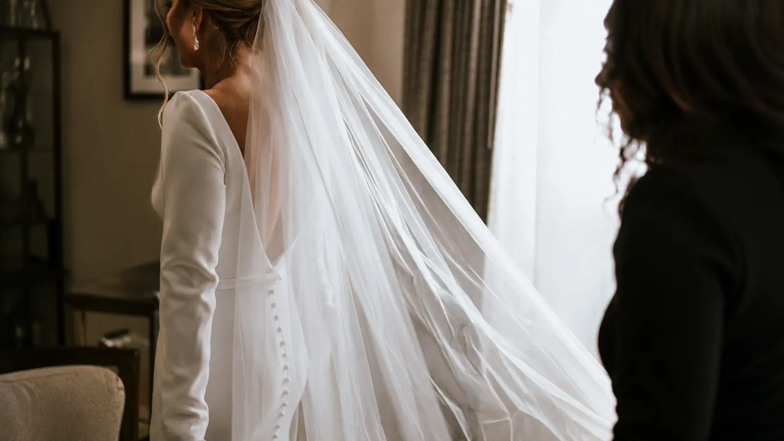 Bride wearing a long simple wedding veil of plain sheer tulle flowing behind a minimalist long-sleeve wedding dress