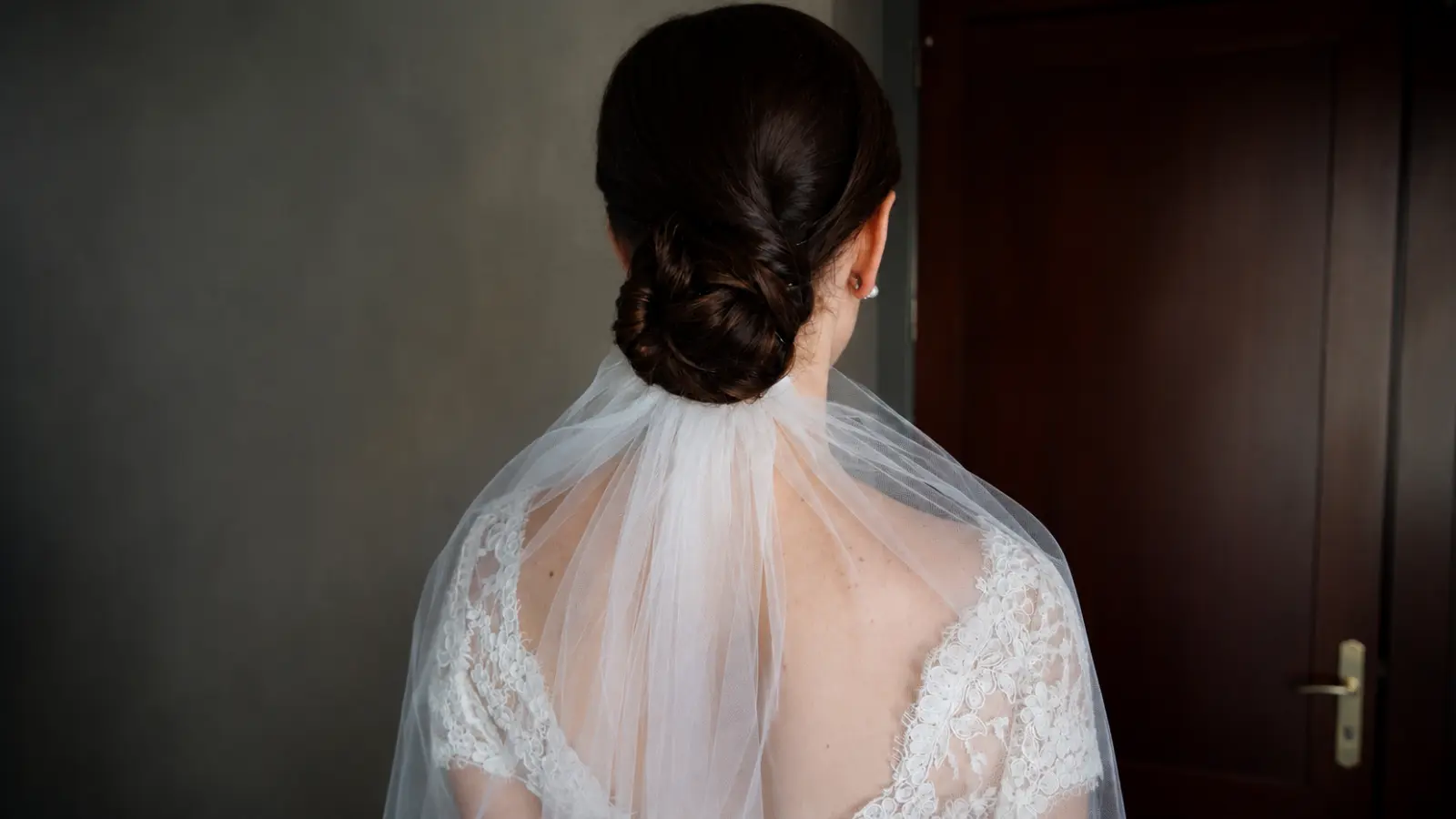 Bride wearing a simple wedding veil beneath a sleek low bun with soft sheer tulle draped across her shoulders