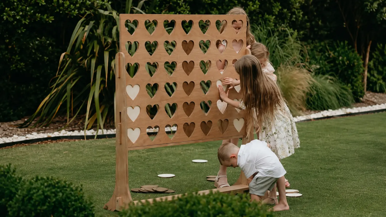 Children playing a large wooden heart game on the lawn, showing an interactive outdoor wedding activity designed to entertain kids during the reception