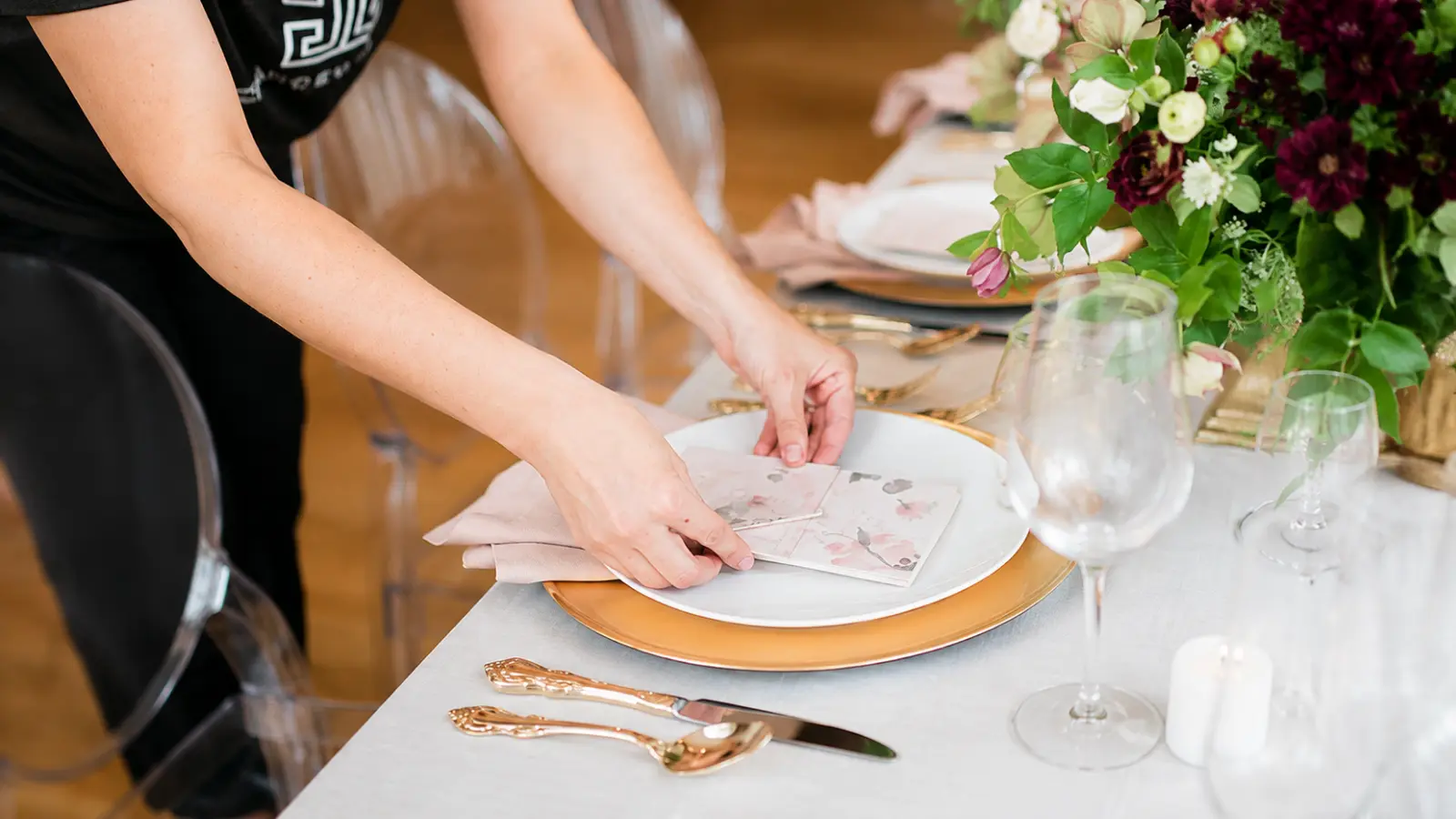 Wedding professional arranging final place setting details on a reception table before guests arrive