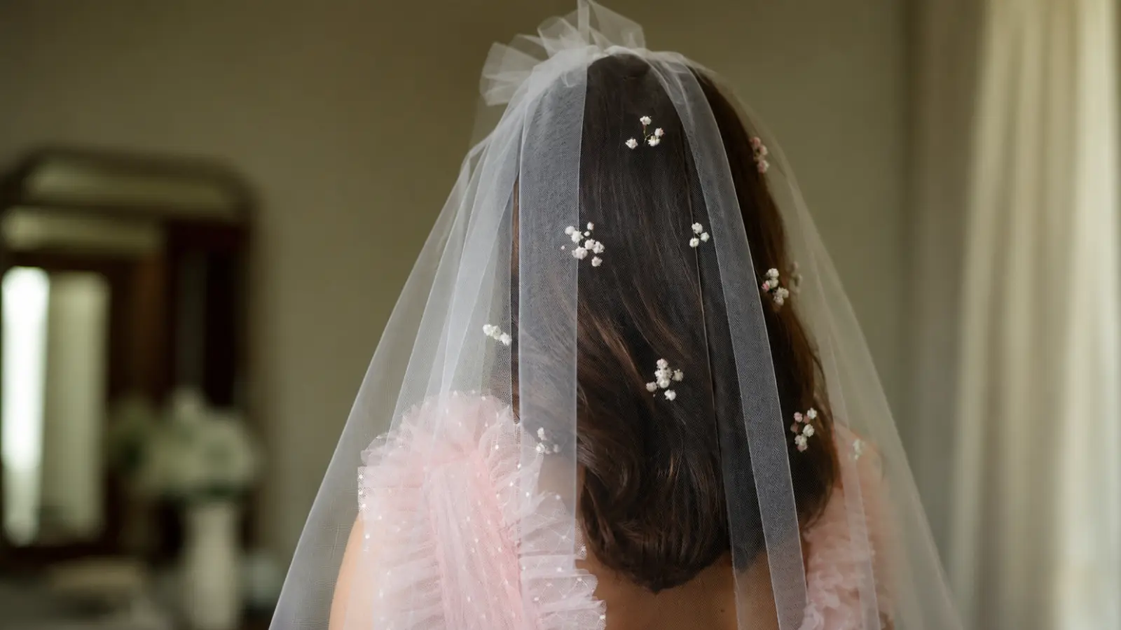 Bride wears softly waved hair down beneath a sheer wedding veil with delicate floral details distributed across the tulle for subtle texture