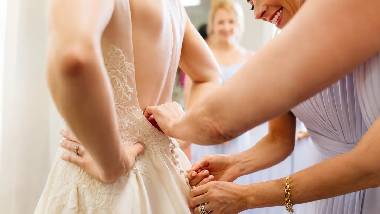 Bridesmaids helping the bride into her wedding dress during a Wedding Morning Timeline that coordinates hair, makeup, getting ready, dressing and photos before the ceremony Wedding Morning Timeline: Hair, Makeup, Getting Ready and Photos
