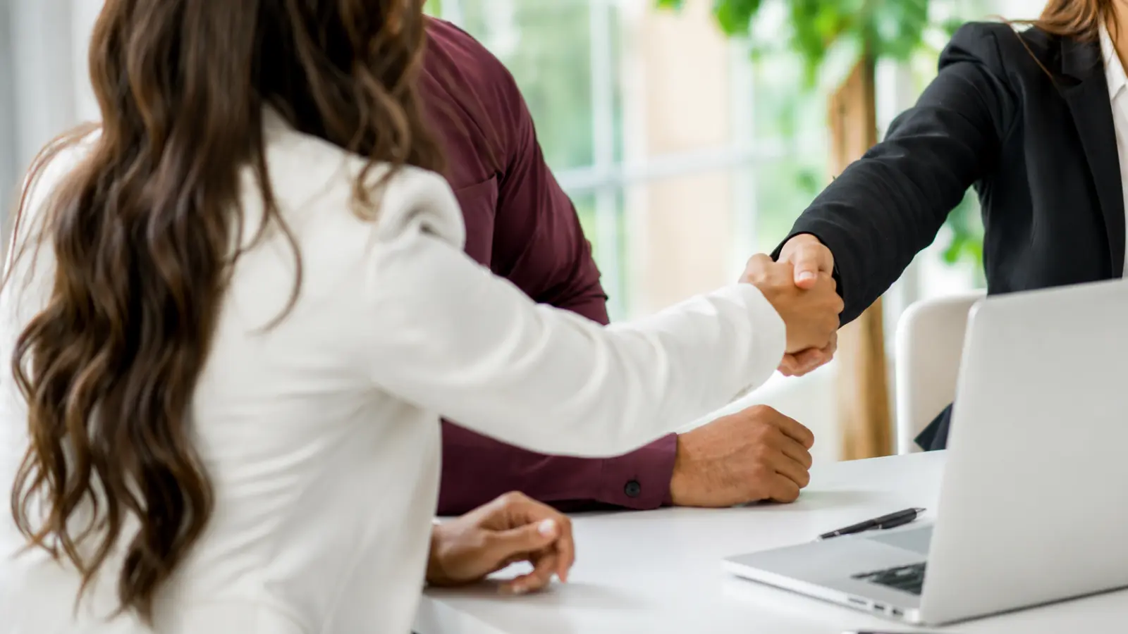 Engaged couple meeting with a wedding professional at a desk and shaking hands while discussing services and details for their upcoming wedding