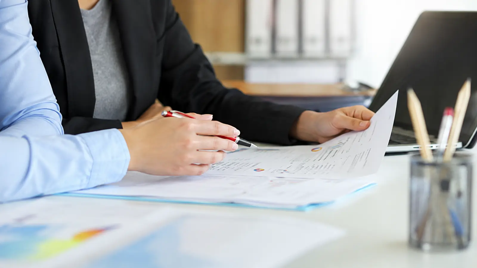 Couple reviewing wedding budget documents with a professional at a desk while discussing costs, contracts and other important details for their wedding