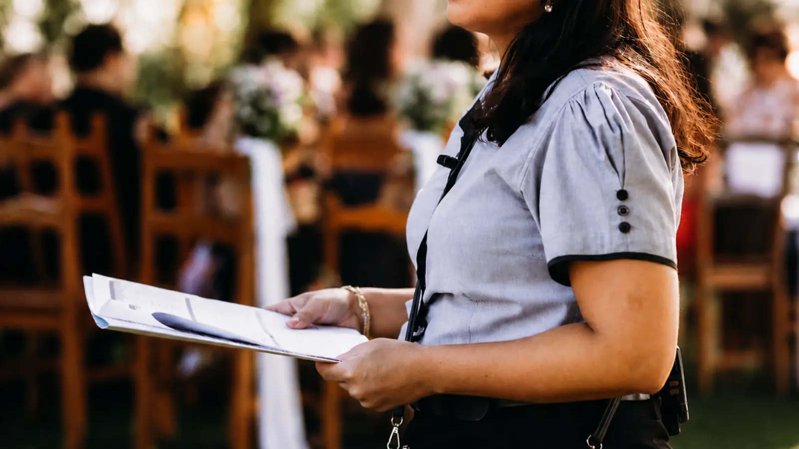 Wedding coordinator holding a planning checklist while reviewing final reception details with decorated guest seating visible in the background Wedding Reception Checklist: What to Book, Decide and Confirm