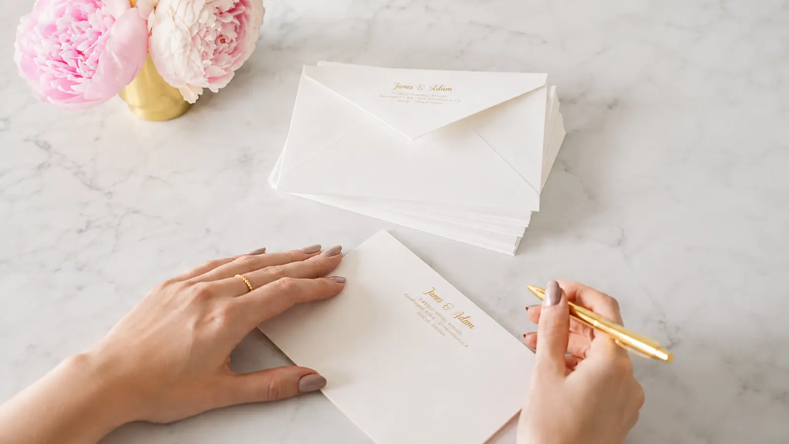 Wedding thank you card envelopes being addressed by hand with a gold pen before personalized cards are mailed to wedding guests