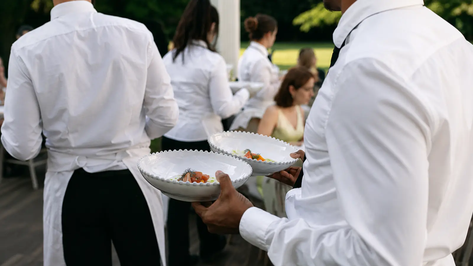 Wedding Vendors catering staff carrying plated dishes while serving guests during an outdoor wedding reception