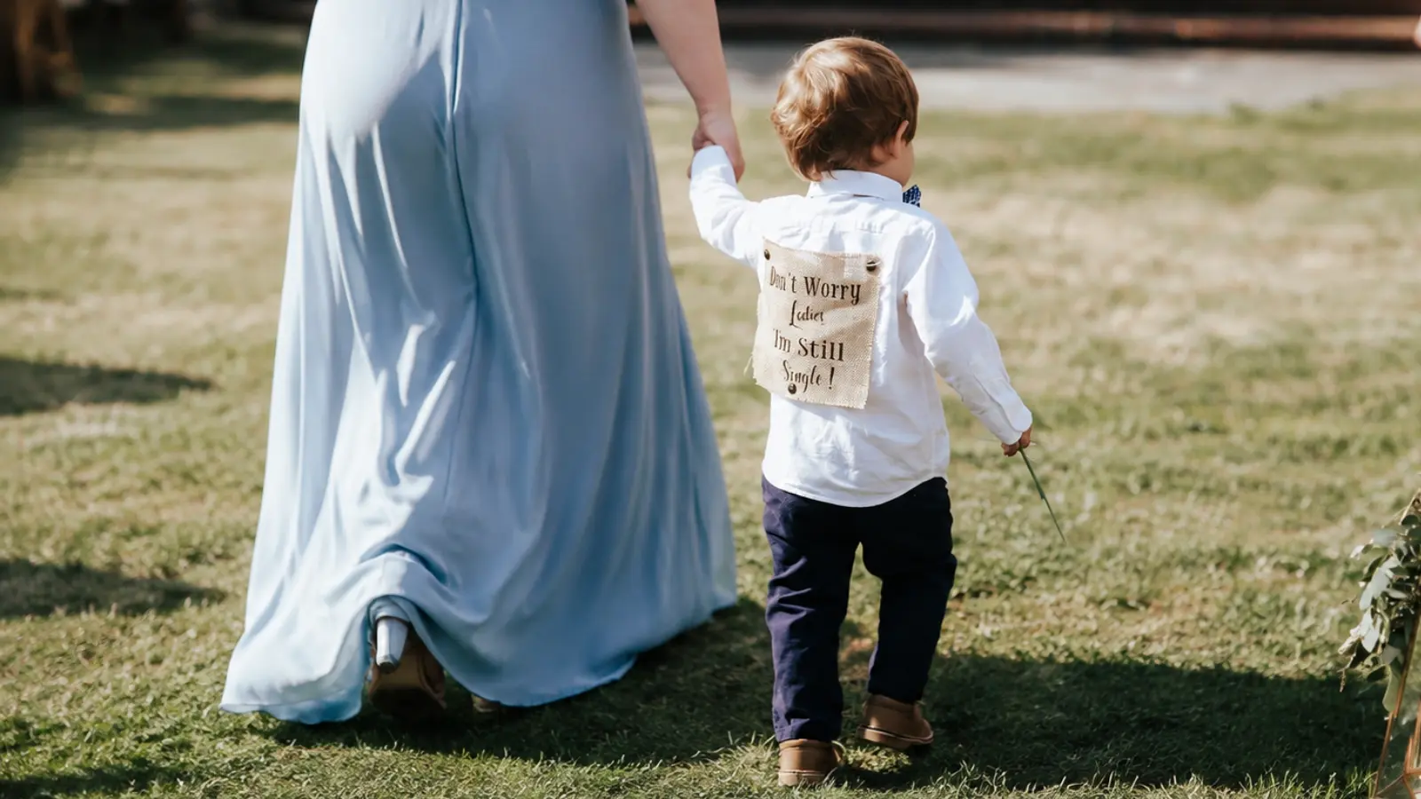 Young ring bearer walks hand in hand with an adult toward the wedding ceremony, showing how younger children can receive help during the processional Ring Bearer Duties