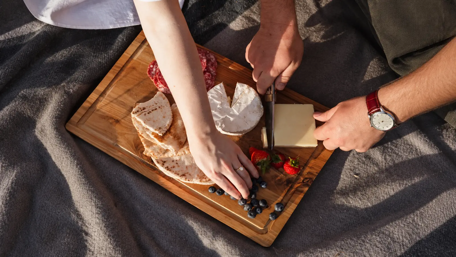 Couple preparing a picnic on a wooden serving board, illustrating a shared experience inspired by the traditional wood fifth anniversary theme