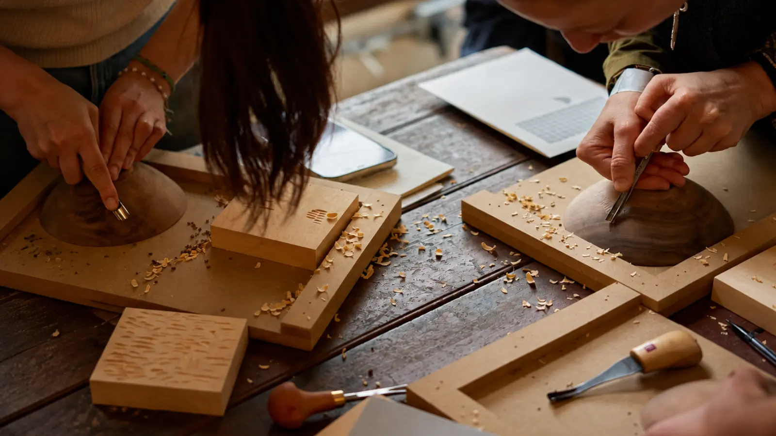 Couple carving wooden pieces together during a woodworking class, illustrating a creative experience gift for a fifth wedding anniversary