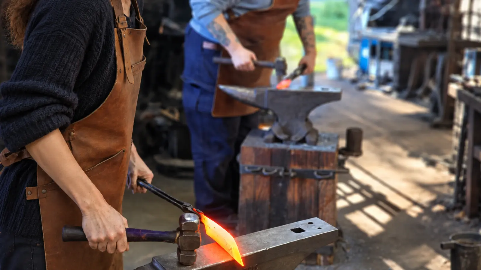 Couple participating in a blacksmithing workshop with hot iron and anvils, illustrating an experience gift for a sixth wedding anniversary