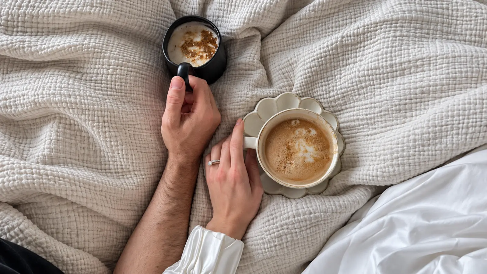 Couple sharing coffee together under a textured blanket as a cozy 9th wedding anniversary gift and celebration idea