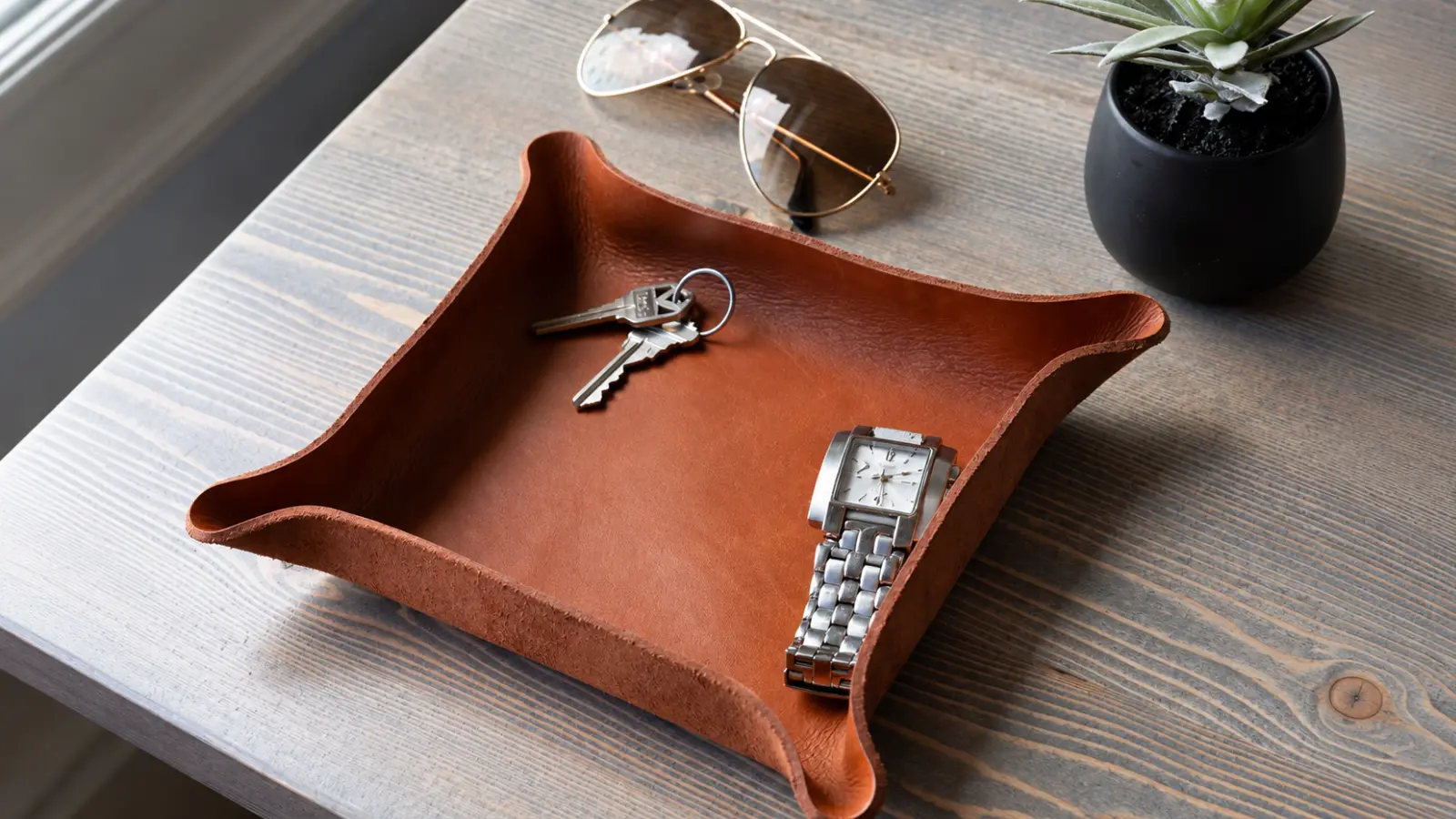 Watch and personal accessories arranged on a leather tray, illustrating modern wedding anniversary gifts and presents traditionally associated with anniversary years