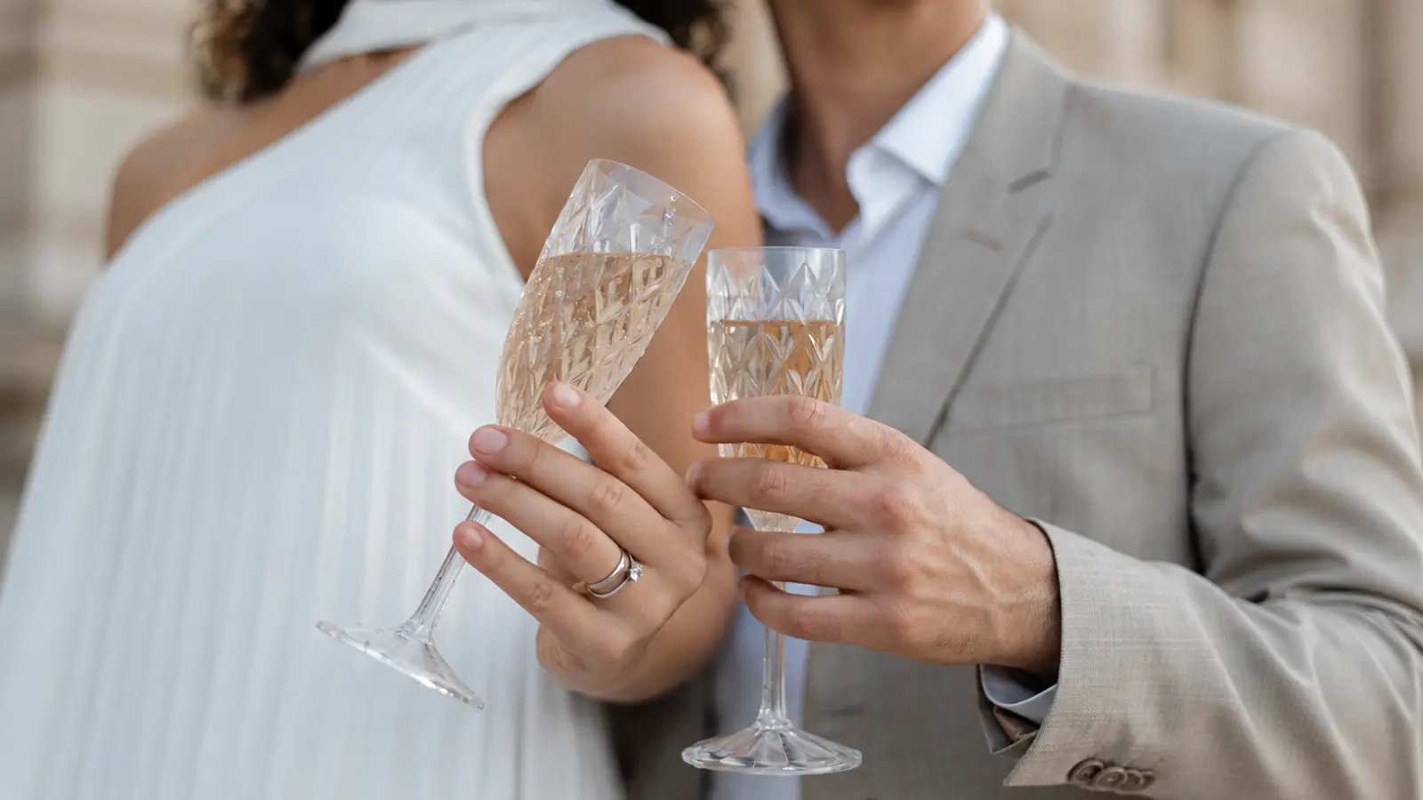 Married couple with wedding rings raising champagne glasses together to celebrate a wedding anniversary milestone