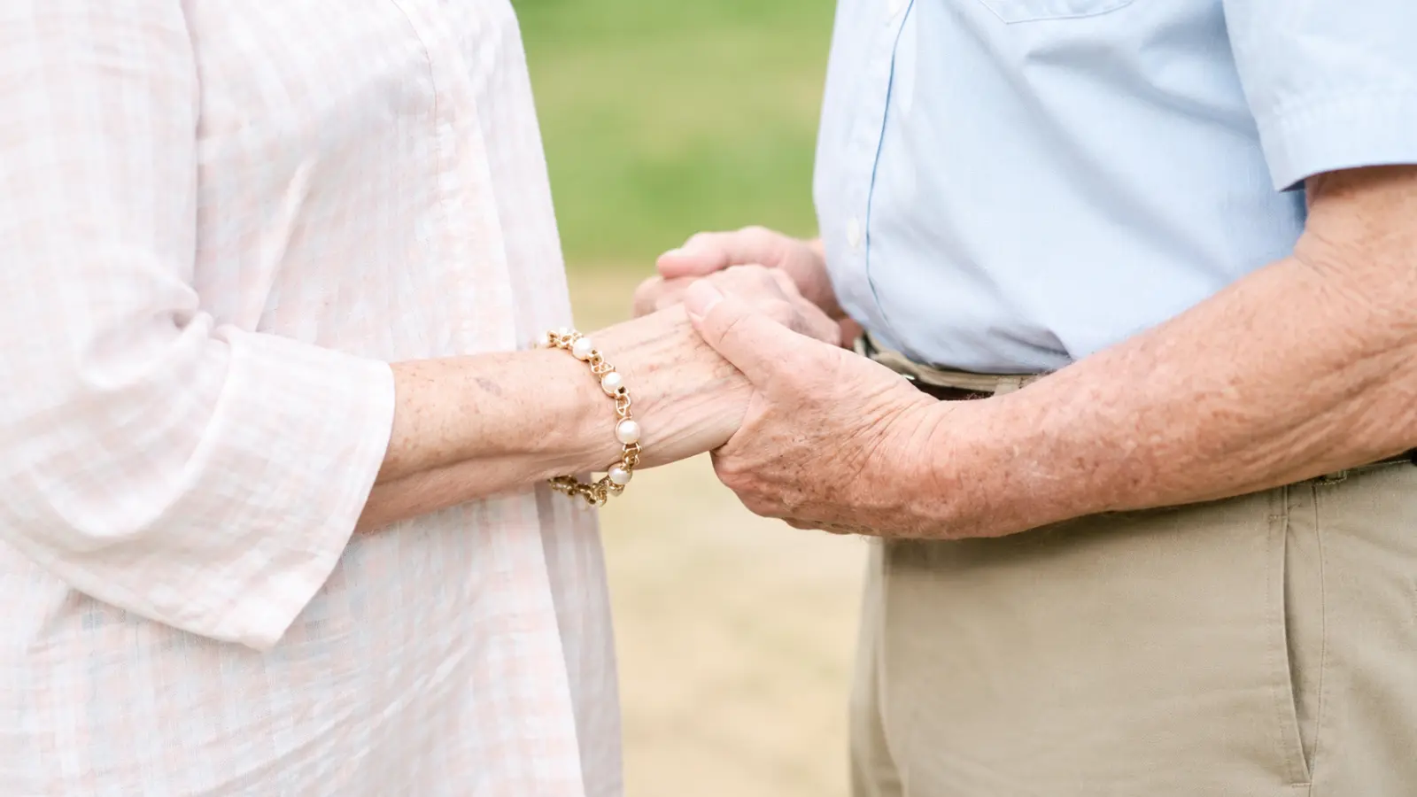 Older married couple holding hands outdoors, illustrating lasting love, companionship and meaningful wedding anniversary milestones
