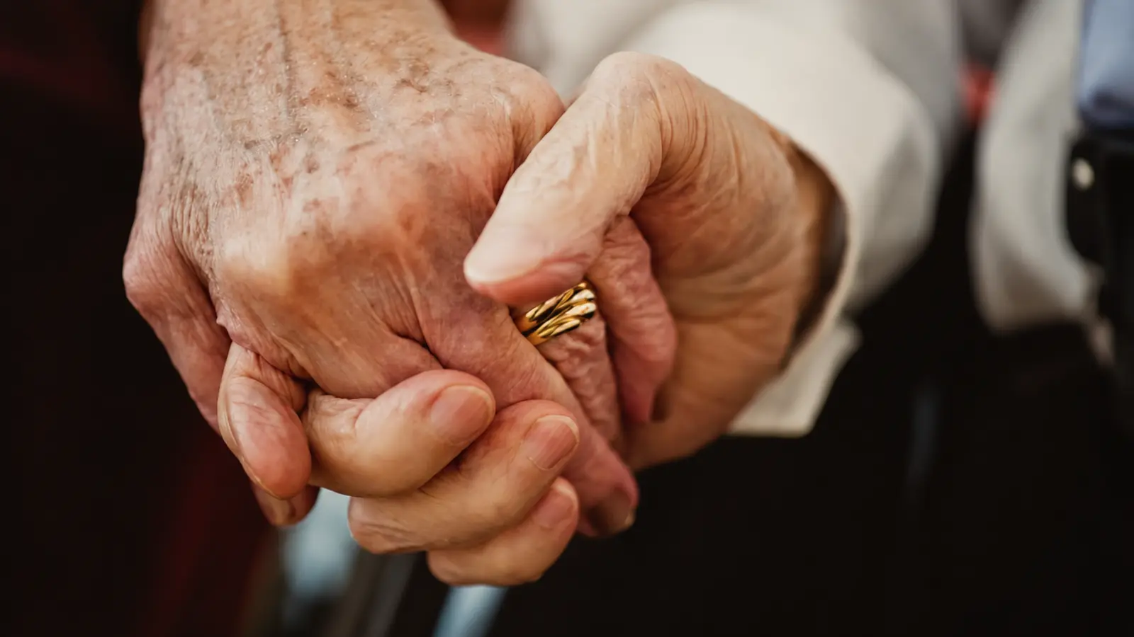 Older married couple holding hands with a gold wedding ring visible, illustrating decades of marriage and traditional wedding anniversary milestone names