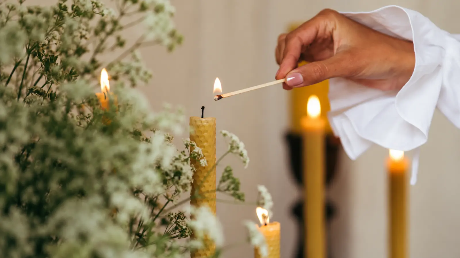 Hand lighting a natural beeswax candle among flowers, illustrating the traditional wax theme for a 16th wedding anniversary gift