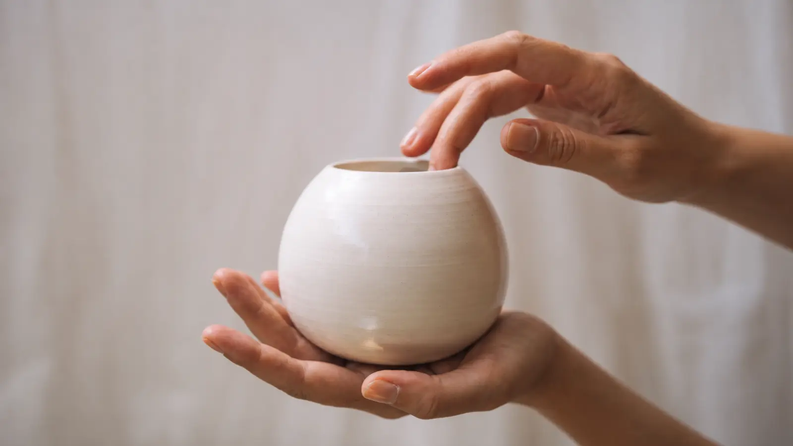 Hands holding a delicate white porcelain vessel, representing porcelain as the traditional 18th wedding anniversary gift theme
