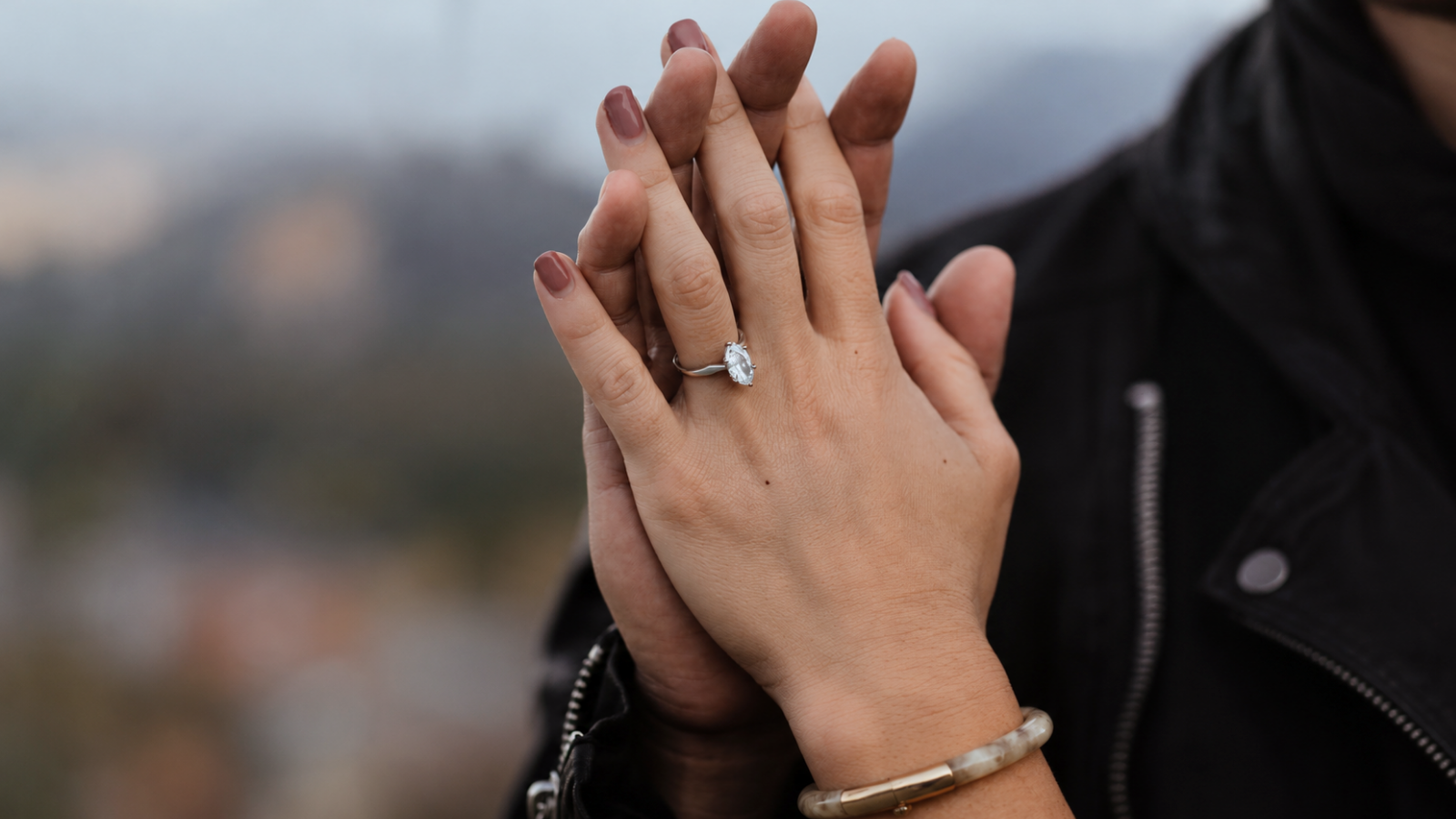 Close-up of a couple gently pressing their hands together outdoors, with a gemstone ring visible, representing love and lasting commitment across the 21st through 24th wedding anniversaries 21st–24th Wedding Anniversary Gifts: Brass, Copper, Silver Plate and Music