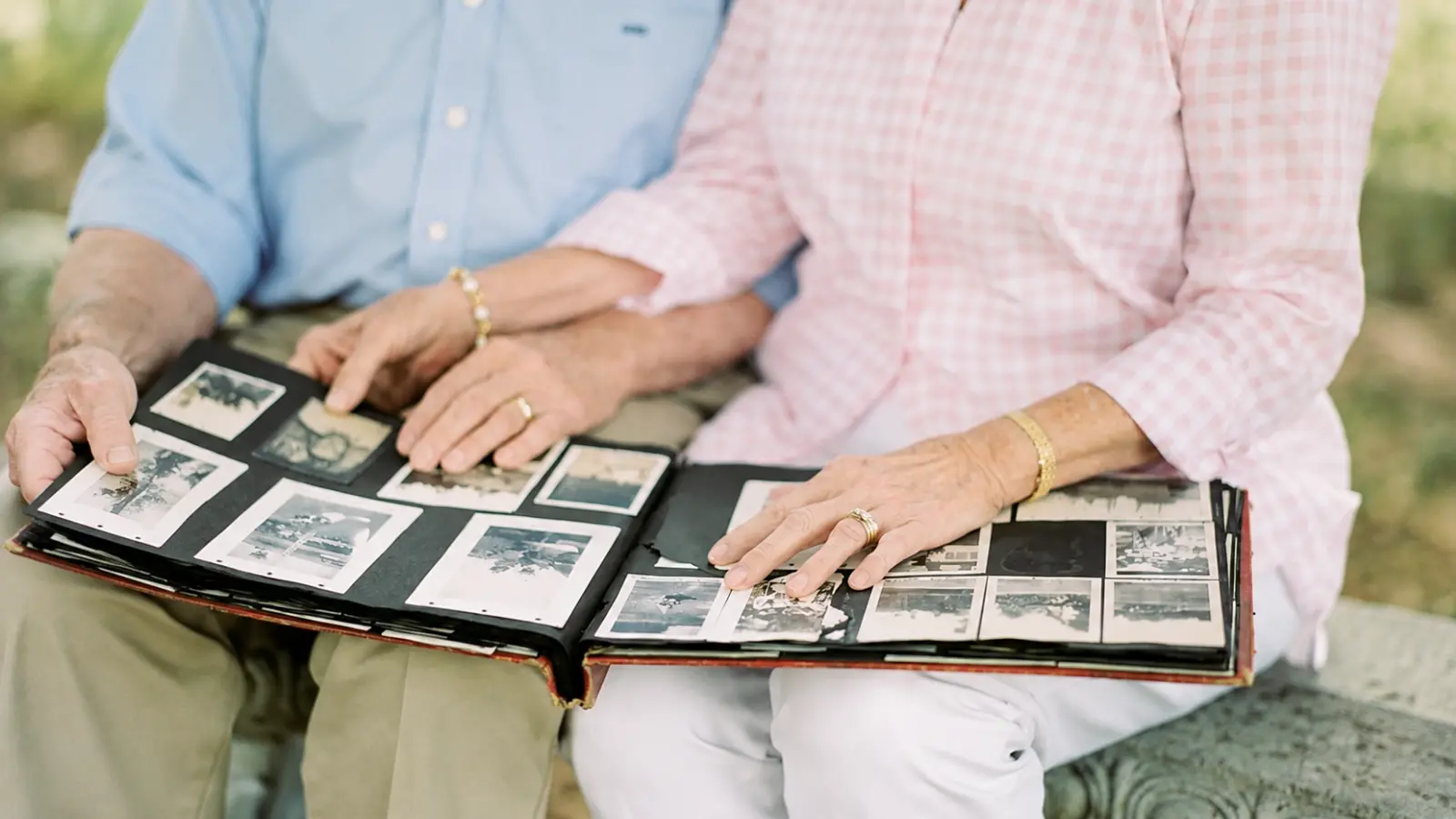 Older couple sitting closely together outdoors while looking through a large photo album filled with vintage photographs, representing meaningful memories shared over thirty years of marriage