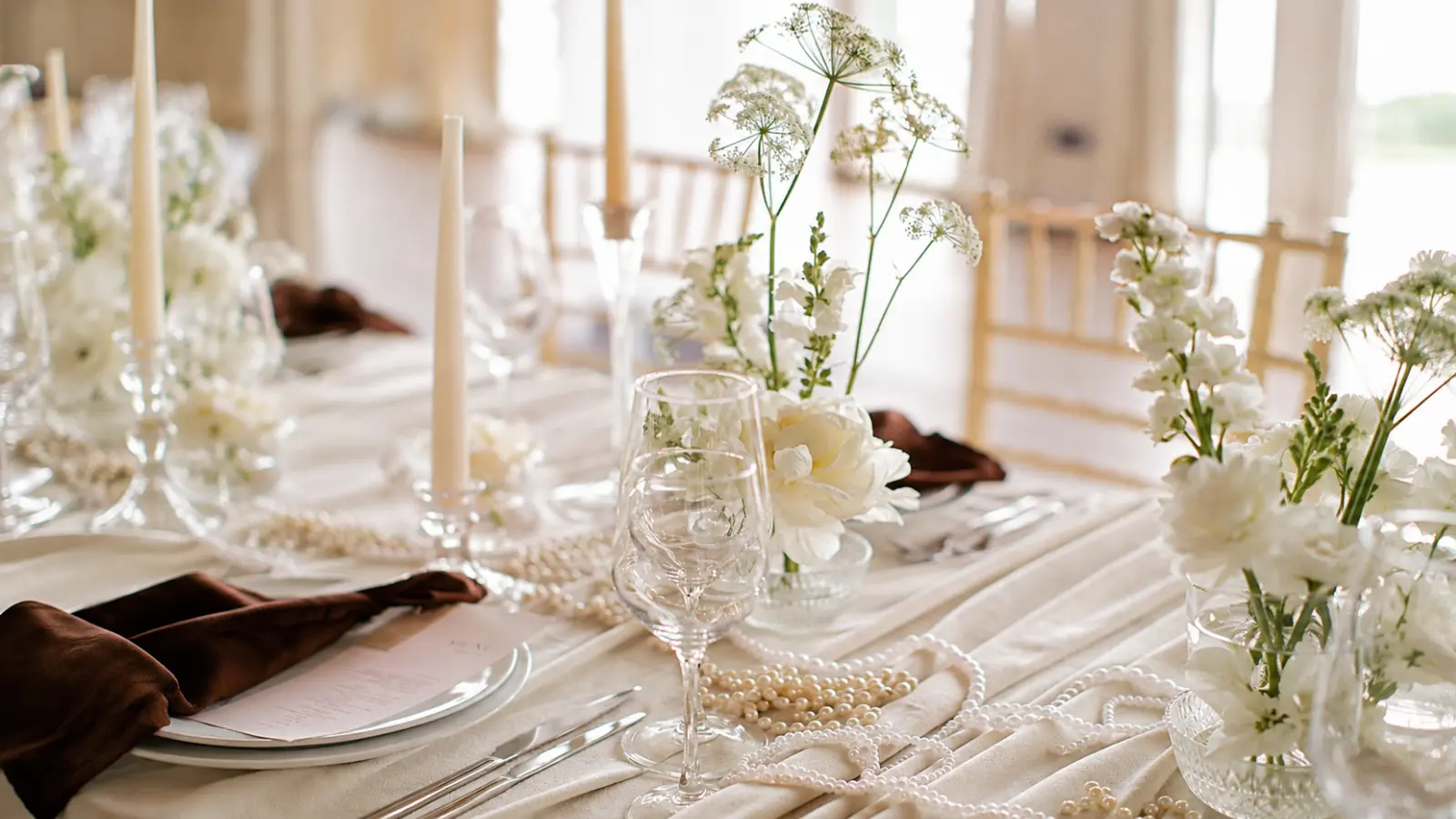 Elegant anniversary dining table decorated with white floral arrangements, ivory candles, delicate pearl strands and glassware, creating a romantic setting for a 30th wedding anniversary celebration
