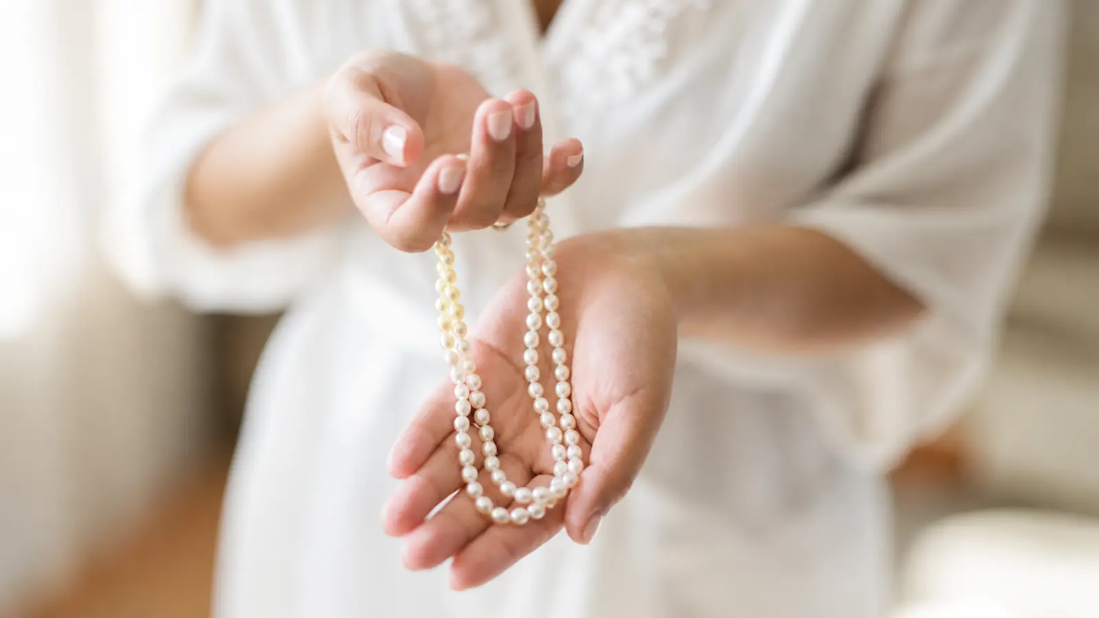 Woman gently holding a delicate strand of white pearls in both hands, illustrating a classic pearl necklace as a traditional 30th wedding anniversary gift